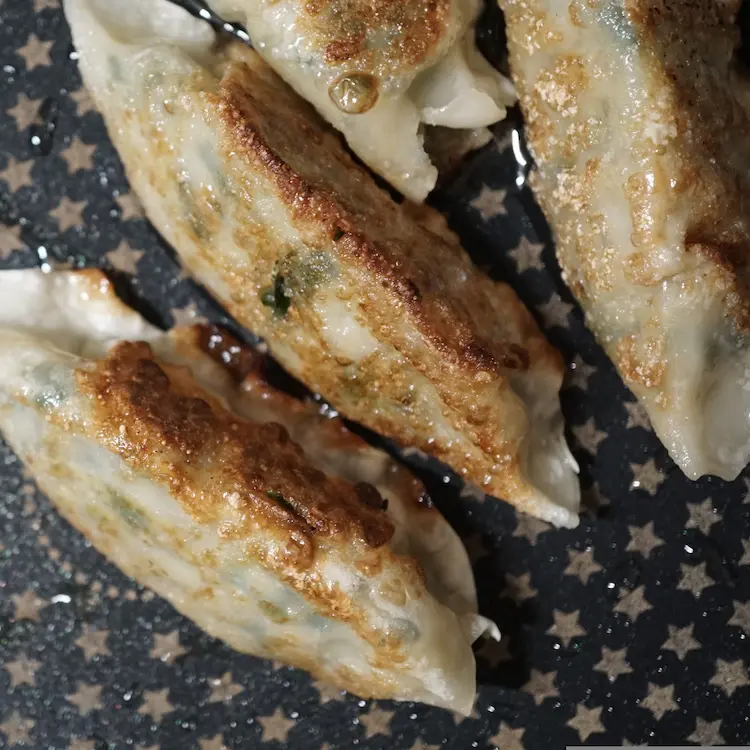 Four crispy and brown pork gyozas sizzle in oil on a pan.